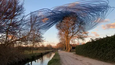 A water filled ditch, reflecting the sky, and a gravel road go straight into one point in the middle of the horizon. The camera is pointing up a bit. Trees to the left are dark, but the trees to the right of the road bathe in orange light of a sunset. Starlings approach these trees. Some dive right into it, others decide to do a go-around first.
Since the camera was on a tripod, I was free to bike into the frame. When I was under the trees, I got shat on.