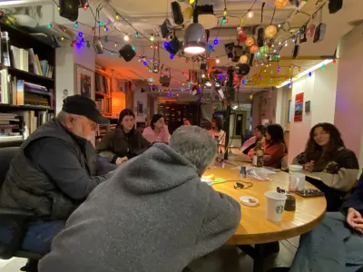 Frank Armstrong an Stephen DiRado, teaching in their cosy classroom. Stephen is seen from the back. He is so engaged with the class, that he’s partly over the table. Students listen closely. Colourful Christmas lights dangle from the ceiling.