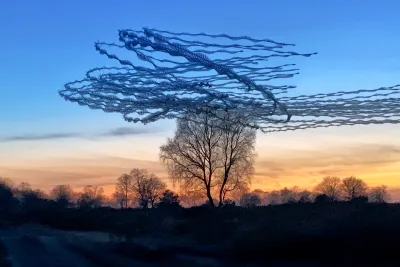 Dusk. The sky is blue at the top, but orange at the horizon. The horizon shows many silhouettes of trees in the far background. There is a double stemmed tree in the front. The crows left the tree in two groups. One flew to the right immediately, the other flew a circle first. In the image, the crows flying straight have exited the frame, while the circling crows have only just completed one turn.