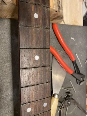 The surface of the fretboard is rough after the removal of the frets. Each fret took some splinters with it. Next to the neck are the red pliers that we used to grap the frets off.